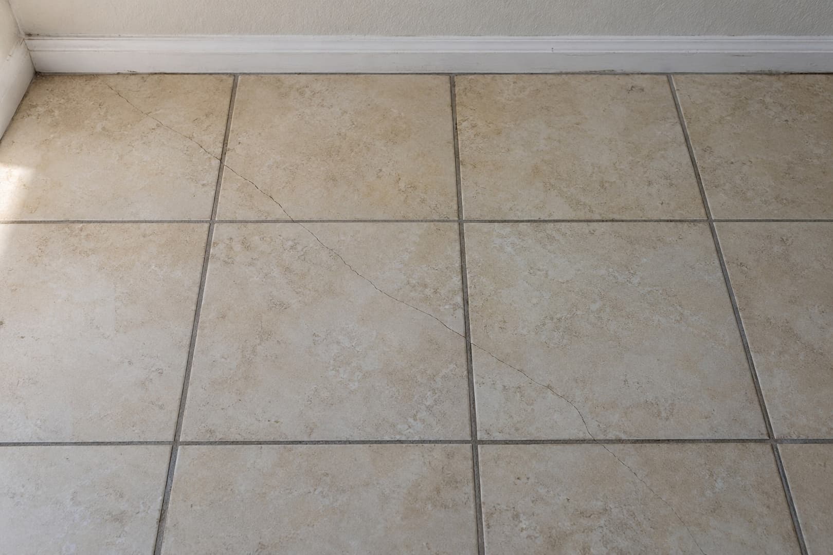 A continuous crack crossing several square floor tiles and their grout joints