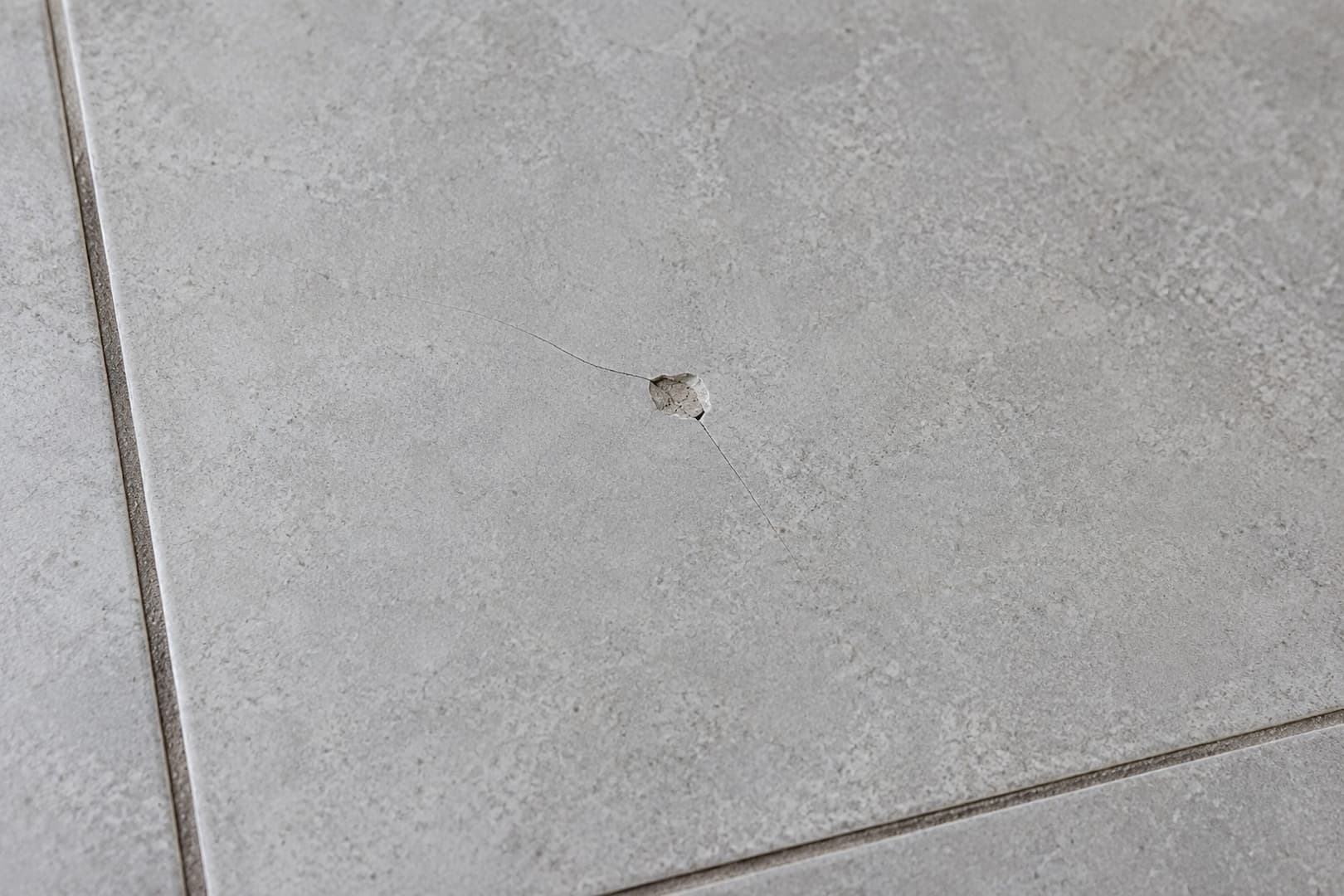 Small impact chip and fine cracks in a light gray porcelain floor tile